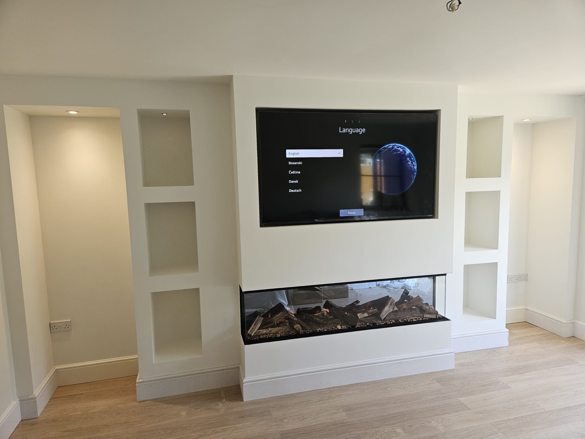 Completed media wall feature with inset TV, full-width fire and lit display niches, fully plastered and decorated